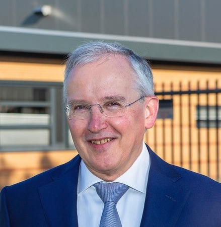 Lachende oudere man met poort en gebouw van De Ploeg Techniek op de achtergrond