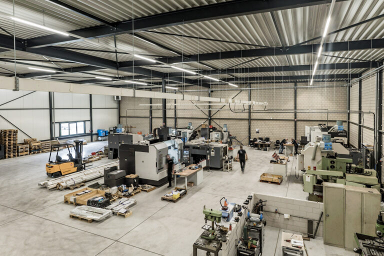 Een moderne fabriekshal met CNC-bewerkingsmachines, werkbanken en een vorkheftruck. Werknemers zijn bezig met machinebediening en kantoorwerk